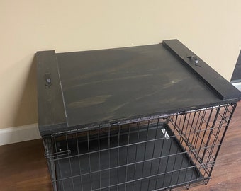 Può includere: Cassa per cani in metallo nero con un coperchio in legno. Il coperchio ha due maniglie sui lati. La cassa è appoggiata su un pavimento in legno.