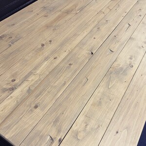 May include: Weathered oak wood tabletop with a light brown stain. The wood grain is visible and the surface is smooth.