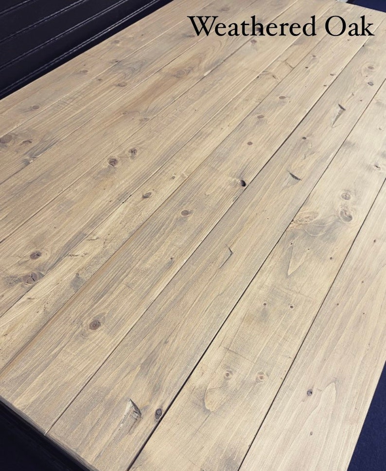 May include: Weathered oak wood tabletop with a light brown stain. The wood grain is visible and the surface is smooth.