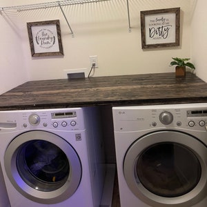May include: A white laundry room with a wooden countertop and two appliances. The appliances are a white washing machine and a white dryer. The dryer is an LG brand. There are two signs on the wall. One sign says "For Same Day Service The Laundry Room Do It Yourself". The other sign says "The laundry is looking at me Dirty Again".