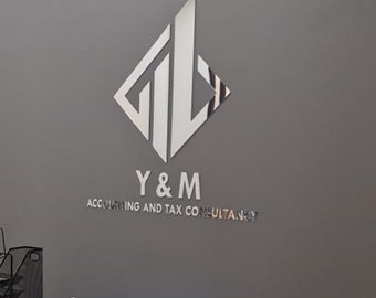 May include: A silver logo of a company, Y & M, is mounted on a gray wall. The logo is a stylized design with geometric shapes. Below the logo, the text "Y & M" is displayed, followed by "ACCOUNTING AND TAX CONSULTANCY".