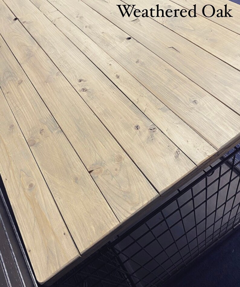 May include: Weathered oak wood tabletop with a light brown colour and a natural wood grain pattern. The wood is arranged in horizontal planks.
