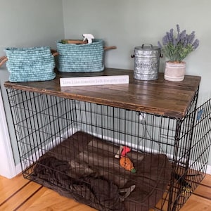 May include: A black wire dog crate with a dark brown wooden top. On the top sit two teal woven rope baskets, a galvanized metal canister with the word DRINKS, a potted lavender plant, and a white sign reading live like someone left the gate open.