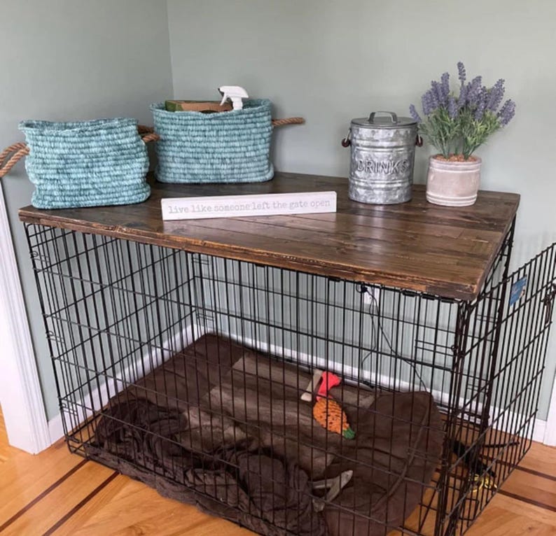 May include: A black wire dog crate with a dark brown wooden top. On the top sit two teal woven rope baskets, a galvanized metal canister with the word DRINKS, a potted lavender plant, and a white sign reading live like someone left the gate open.