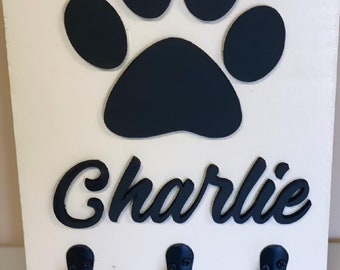 May include: White wooden key holder with a black paw print and the name "Charlie" in black lettering. Three black hooks are attached to the bottom of the holder.