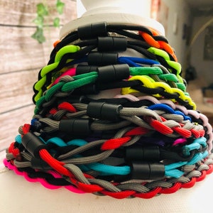 Pu&ograve; includere: Una collezione di collane o braccialetti in paracord intrecciato con una variet&agrave; di colori vivaci tra cui verde neon, arancione, blu, rosso, rosa e grigio. Ogni pezzo &egrave; fissato con una chiusura magnetica cilindrica nera.