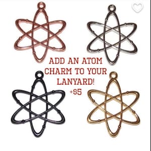 Pu&ograve; includere: Quattro ciondoli in metallo a forma di atomo con finiture in oro rosa, argento, nero e oro. Ogni ciondolo presenta un occhiello per l'aggancio. Il testo al centro recita: ADD AN ATOM CHARM TO YOUR LANYARD! +$5. Design di tipo scientifico.