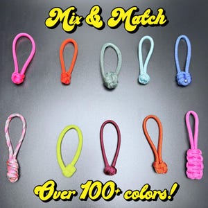 May include: A collection of colorful zipper pulls in various shades, including pink, orange, green, and blue, arranged on a gray surface. The text "Mix & Match" and "Over 100+ colors!" are displayed in a yellow, stylized font.
