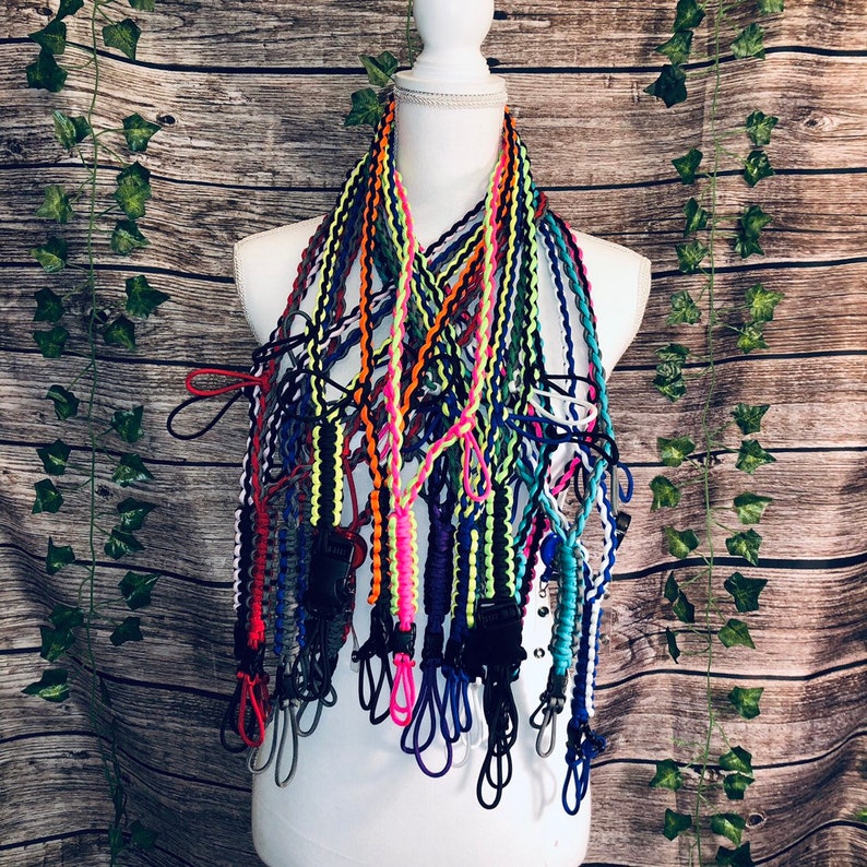 Pu&ograve; includere: Una collezione di molteplici cordini in paracord con design intrecciati in vari colori neon e solidi, tra cui arancione, giallo, blu, nero e rosa. Ogni cordino &egrave; dotato di una fibbia in plastica nera e di un occhiello.