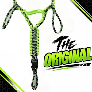 Pu&ograve; includere: Un cordino in paracord con un motivo intrecciato nero e verde neon, dotato di una fibbia centrale in plastica nera. Il design include molteplici anelli e una struttura a forma di Y. Il testo THE ORIGINAL &egrave; visualizzato in grandi lettere verdi e nere.
