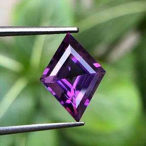 Puede incluir: Una piedra preciosa de amatista de color púrpura oscuro, de forma cuadrada y tallada a facetas.