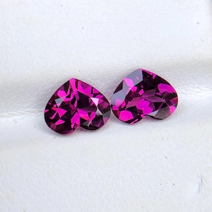 May include: Two heart-shaped pink gemstones, likely amethysts, on a white background.