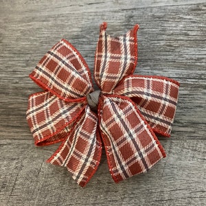 Könnte beinhalten: Eine rote und weiße Karobinde mit einem braunen und weißen Karomuster. Die Schleife ist zu einem Knoten gebunden und hat einen ausgefransten Rand.