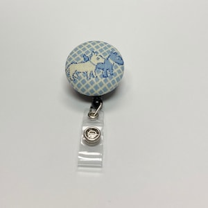 May include: A blue and white patterned fabric button with a black retractable badge holder. The button features a design of two dogs.