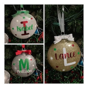 May include: Three personalized Christmas ornaments with glitter and colorful dots. The ornaments are silver, gold, and white with the names "Isabel", "Lance", and "Malcolm" written on them.