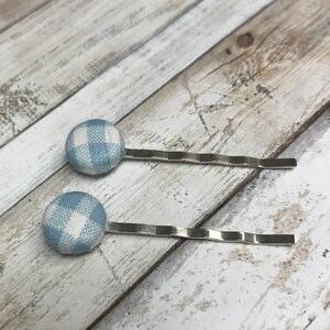 May include: Two silver bobby pins with blue and white gingham fabric buttons attached to the ends.