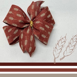 May include: A large red bow with a white wheat pattern. The bow is tied with a gold center piece.