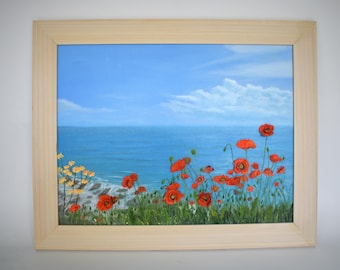Puede incluir: Pintura al óleo de una escena costera con un cielo azul brillante y un océano. Amapolas rojas y flores amarillas florecen en primer plano. La obra de arte está enmarcada en un marco de madera de color claro.