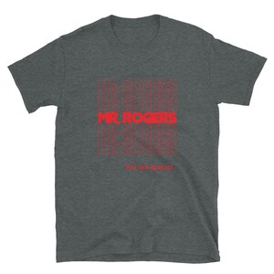 May include: A dark heather grey t-shirt with a red graphic print of the words "Mr. Rogers" repeated multiple times. The text "You are special." is printed below the graphic.
