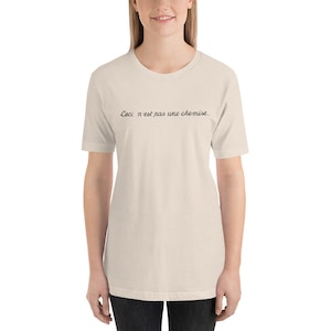 May include: A beige t-shirt with the text "Ceci n'est pas une chemise." printed in black.