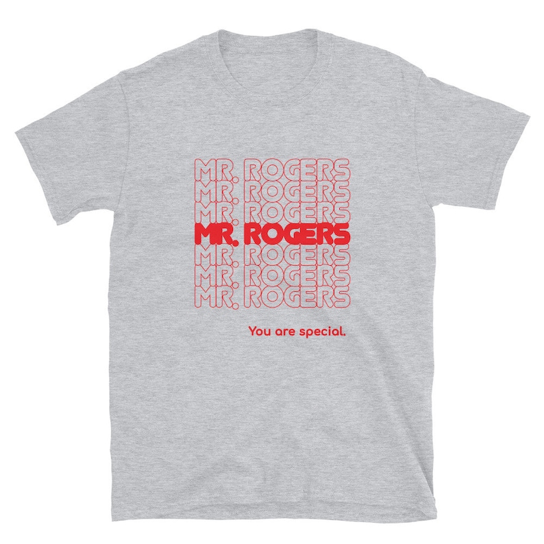 May include: A heather grey t-shirt with a red graphic print of the phrase "MR. ROGERS" repeated multiple times. The text "You are special." is printed below the graphic.