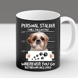 May include: A black and white mug with a white rim and handle. The mug features a cartoon image of a Shih Tzu dog with the text "PERSONAL STALKER I WILL FOLLOW YOU" and a height chart with paw prints. The text "WHEREVER YOU GO BATHROOM INCLUDED" is at the bottom of the mug.