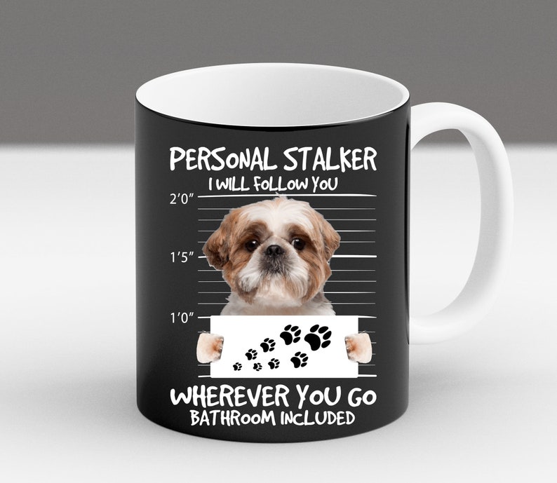 May include: A black and white mug with a white rim and handle. The mug features a cartoon image of a Shih Tzu dog with the text "PERSONAL STALKER I WILL FOLLOW YOU" and a height chart with paw prints. The text "WHEREVER YOU GO BATHROOM INCLUDED" is at the bottom of the mug.
