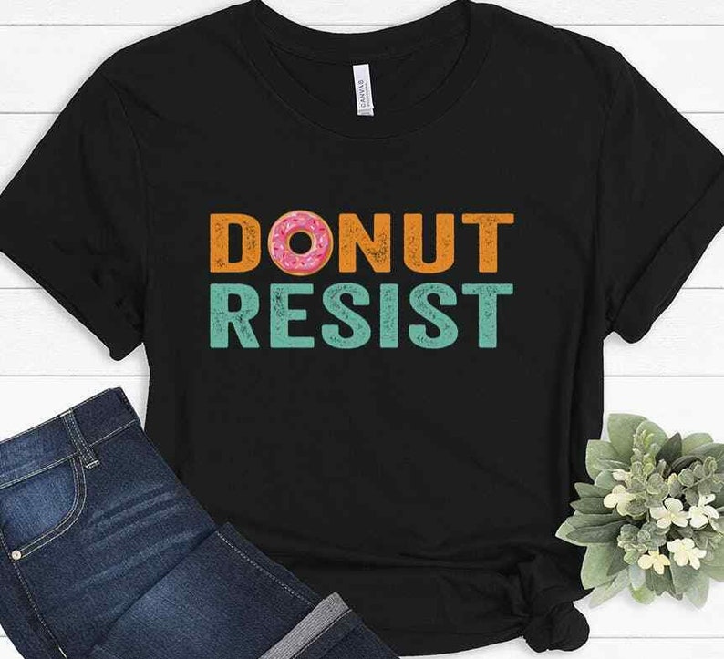 Pode incluir: Camiseta preta com um gr&aacute;fico de estilo vintage que diz "DONUT RESIST" com um donut rosa e branco no meio da palavra "DONUT".