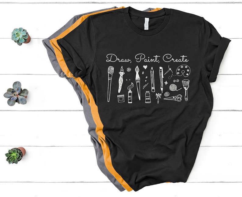 May include: Black t-shirt with a white graphic design of art supplies and the text "Draw, Paint, Create".
