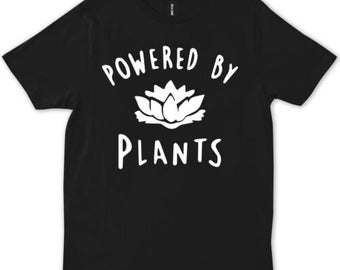 Puede incluir: Camiseta negra con texto blanco que dice "Powered by Plants" y una imagen estilizada blanca de una flor.