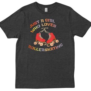 Może przedstawiać: Szary t-shirt z napisem "Just a girl who loves rollerskating" w kolorach tęczy. Tekst znajduje się nad parą czerwonych rolek z żółtymi kółkami.