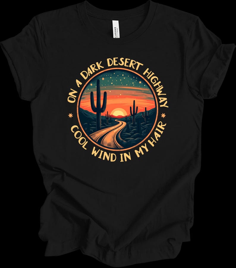 Puede incluir: Camiseta negra con un dise&ntilde;o circular que representa una escena de carretera des&eacute;rtica. El dise&ntilde;o incluye una carretera que conduce a una puesta de sol, cactus y el texto "ON A DARK DESERT HIGHWAY COOL WIND IN MY HAIR."