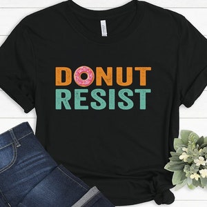 Pode incluir: Camiseta preta com um gr&aacute;fico de estilo vintage que diz "Donut Resist" com um gr&aacute;fico de donut rosa e laranja.