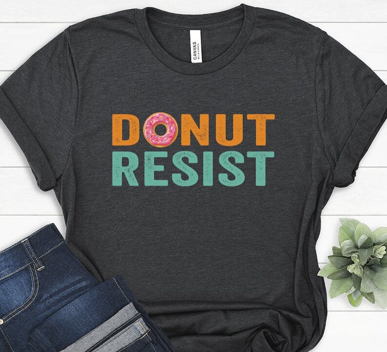 Pode incluir: Uma camiseta cinza escura com o texto "DONUT RESIST" em laranja e turquesa. Um donut rosa e laranja est&aacute; no meio da palavra "DONUT".