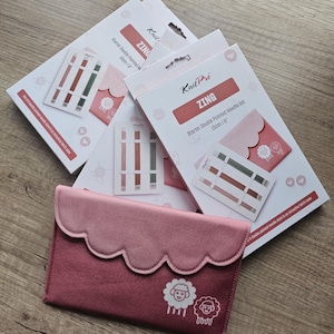 Könnte beinhalten: KnitPro ZING Starter-Stricknadel-Sets mit doppelter Spitze, 15 cm lang, mit einem rosa Stoffetui. Die Verpackung ist weiß mit roten Akzenten und zeigt Abbildungen der Nadeln. Das Etui hat einen gewellten Rand und Schafgrafiken.