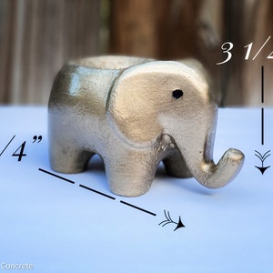 May include: A silver-colored concrete elephant planter measuring 5 1/4 inches long and 3 1/4 inches tall.