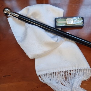 May include: A white paisley scarf with a fringe, a black cane with a silver ball handle, and a box of silver tie clips. The scarf and tie clips are white. The cane is black.