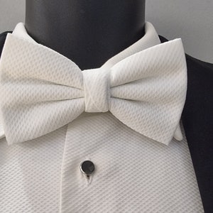 May include: A white bow tie with a textured pattern. The bow tie is tied and ready to wear.
