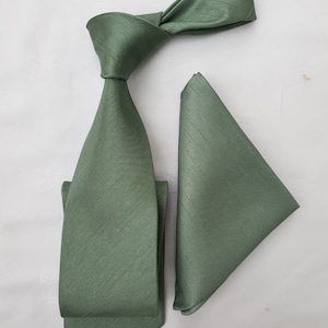 May include: A sage green silk tie and pocket square set. The tie has a classic shape and the pocket square is a simple square.
