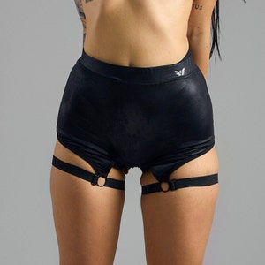 May include: Black shorts with a shiny finish and a small logo on the waistband. The shorts have adjustable straps with rings on the thighs.