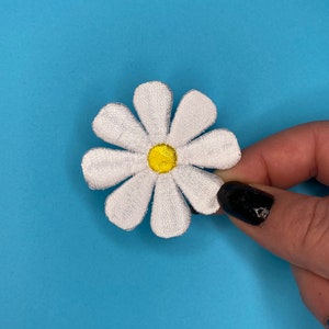 May include: White embroidered daisy flower patch with a yellow center.