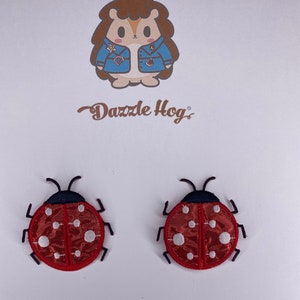 Könnte beinhalten: Zwei rote und weiße Bügelbilder in Form von Marienkäfern mit schwarzen Umrissen und weißen Punkten.