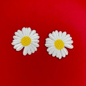 May include: Two white daisy flower patches with yellow centers on a red background.