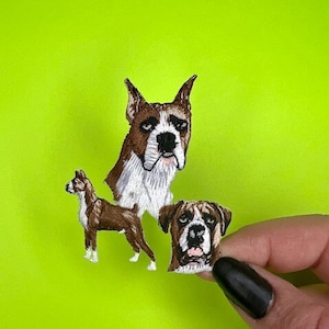 May include: Three embroidered iron-on patches featuring boxer dogs. The patches are brown, white, and black. The largest patch shows a boxer dog's head, the medium patch shows a boxer dog standing, and the smallest patch shows a boxer dog's head.