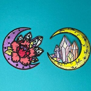 May include: Two embroidered iron-on patches featuring crescent moons with different designs. One moon has a pink flower with crystals, the other has colorful crystals.