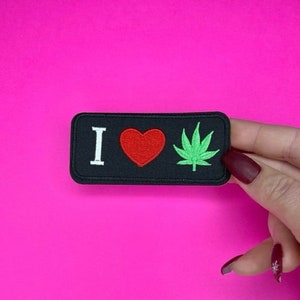 May include: Black patch with white text that says "I love" and a red heart. A green marijuana leaf is to the right of the heart.