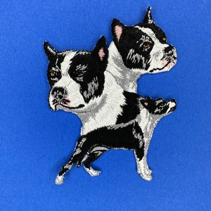 May include: Embroidered patch featuring a stylized dog design in black, white, and gray. The patch depicts the dog's head and body, with detailed stitching and a blue background.