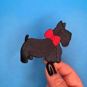 Könnte beinhalten: Schwarzer gestickter Bügelaufkleber mit einem schottischen Terrier, der eine rote Schleife trägt.