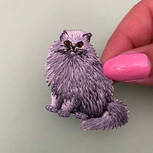 Può includere: Toppa ricamata di colore viola con un gatto soffice con occhi neri.