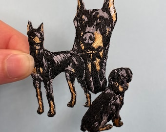 May include: Three embroidered iron-on patches of black Doberman Pinschers in different poses. The patches are perfect for adding a touch of personality to clothing, bags, or other fabric items.